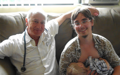 Dr. Newman, wearing a stethoscope, sits beside me on a couch as I nurse Jacob.