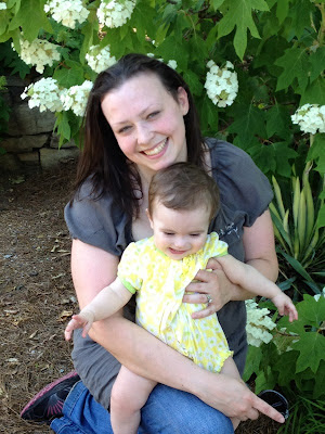 Mom and baby sharing a happy moment next to a flowering bush.