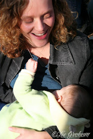 Lisa smiles down at her baby as she breastfeeds. Her baby grasps Lisa's necklace.