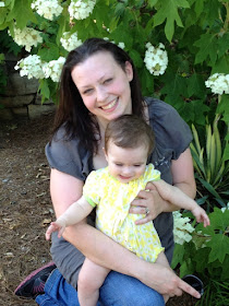 Mom and baby sharing a happy moment next to a flowering bush.